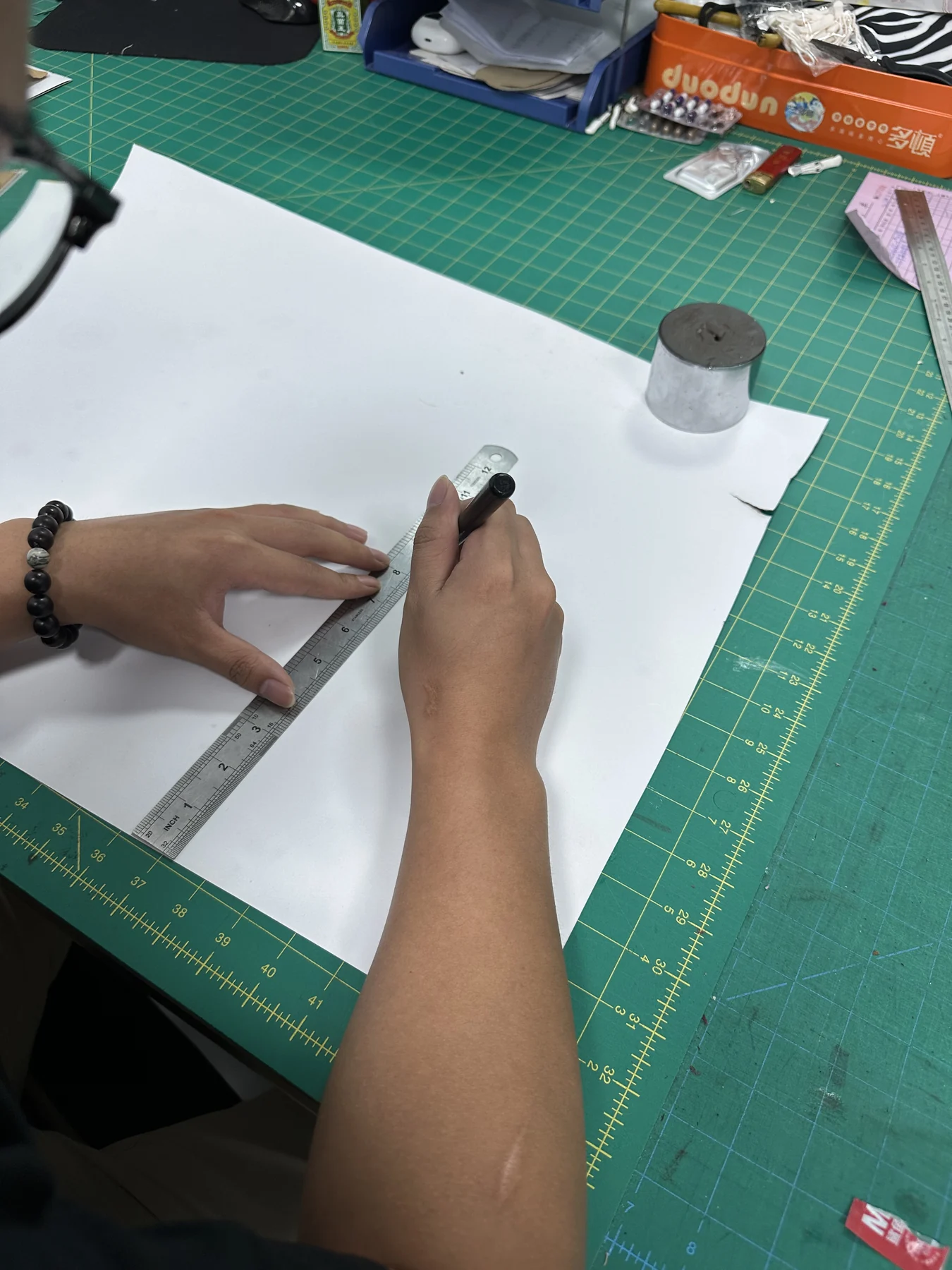 Hongzhao bag pattern maker checking measurements on a paper pattern over a gridded cutting mat